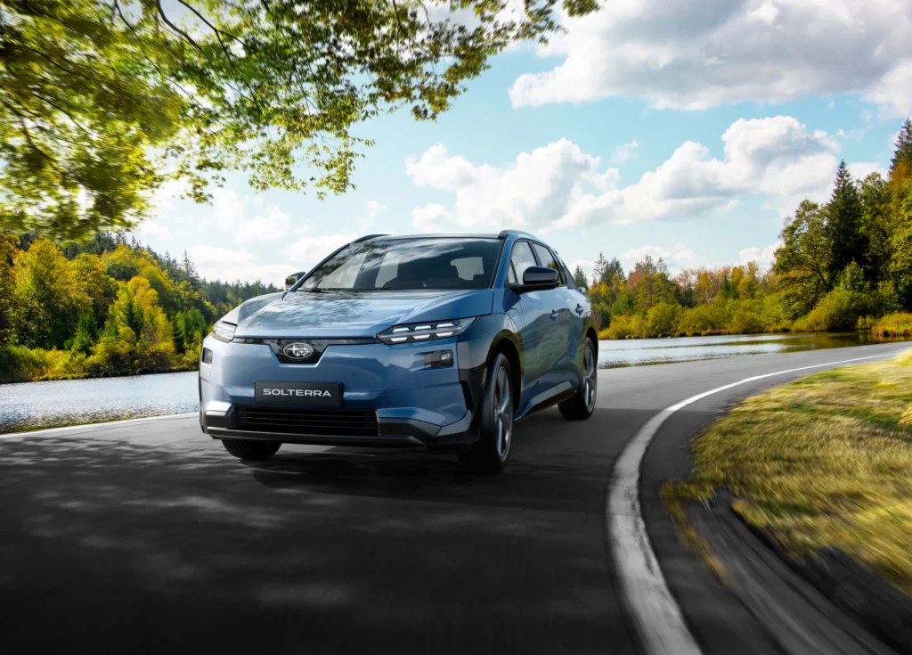 Blå Subaru SUV kjører på vei ved elv og trær.