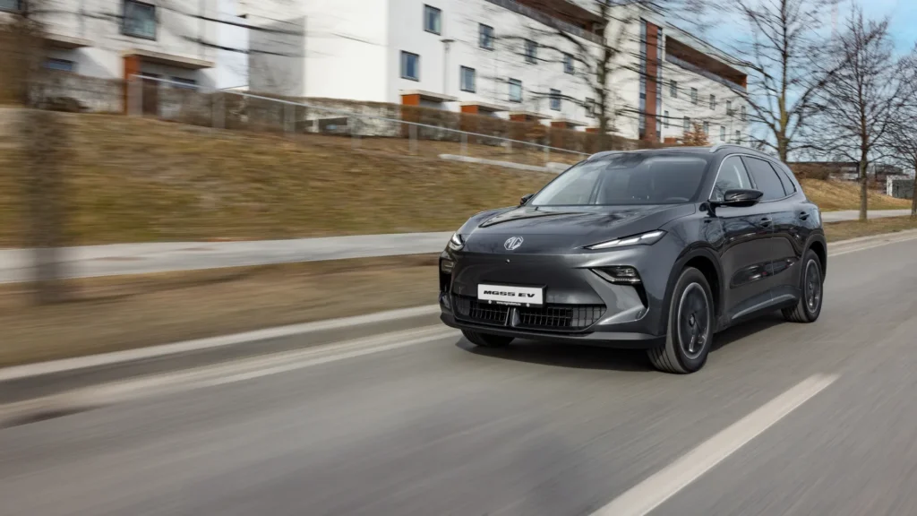 Svart elbil kjører på vei ved boligblokker og trær.