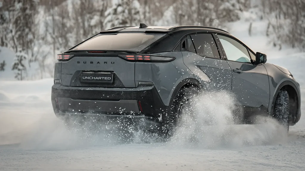 Grå SUV kjører gjennom snø i en vinterlig skog.