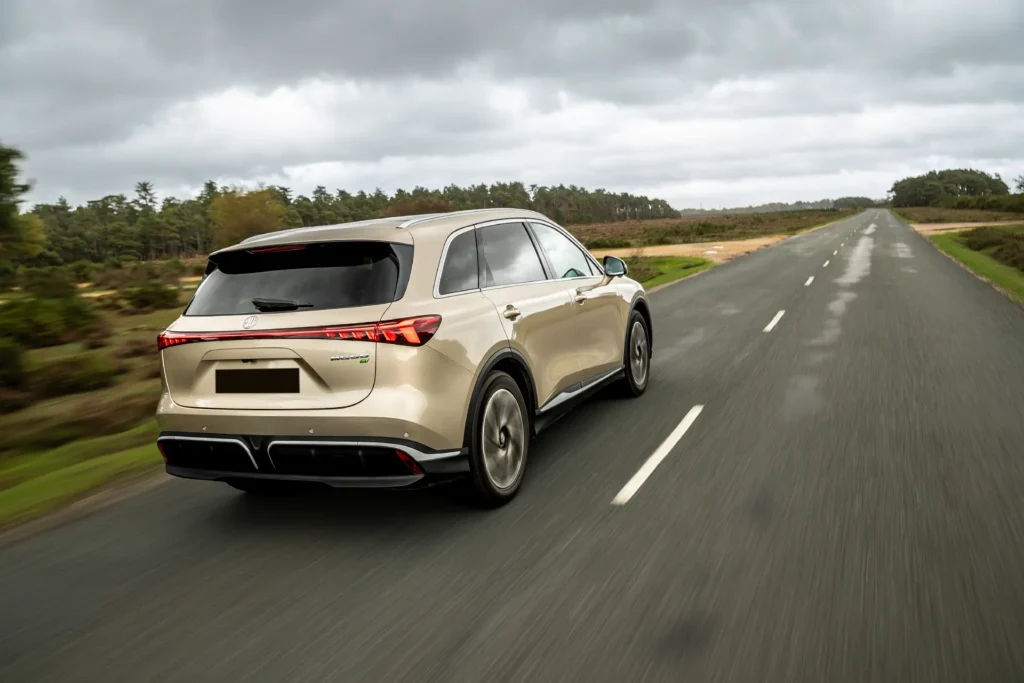 Beige SUV på tom landevei med trær og gress.