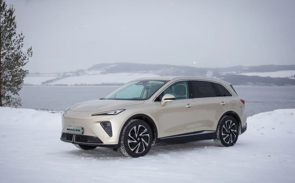 Beige MGS6 parkert i snø ved innsjø og trær om vinteren.