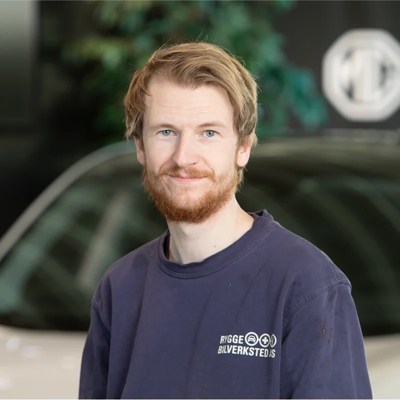 En mann med skjegg i blå kontakt moss autocenter-skjorte innendørs.