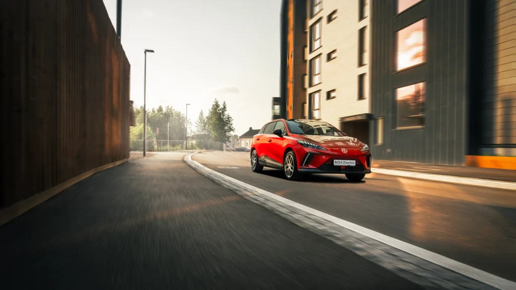 Rød bil kjører på tom, svingete gate med moderne bygninger.